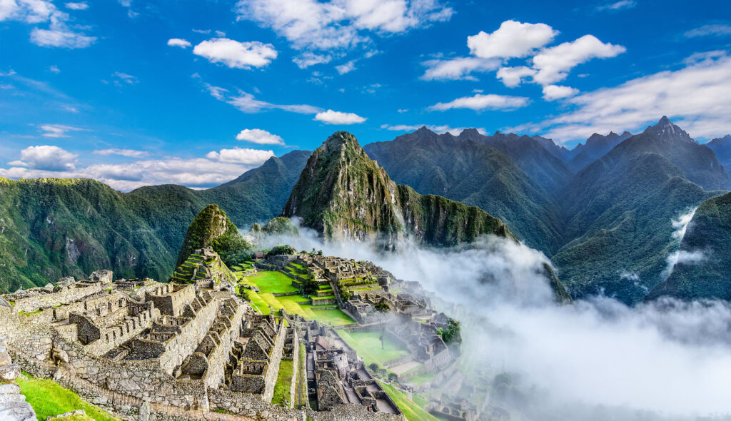 Aerial view of the ancient Inca citadel of Machu Picchu emerging from morning cloud mist in the Peruvian Andes, with Huayna Picchu mountain rising dramatically behind the stone ruins.